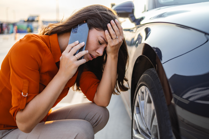 women on the side of the road with a flat tire calling for assistance